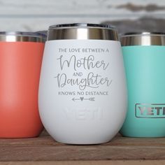 three different colored yeti tumblers sitting on top of a wooden table with the words, the love between mother and daughter knows no distance