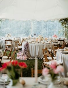 tables set up in a tent with white tablecloths and pink flowers on them