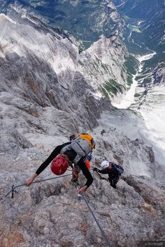 two people climbing up the side of a mountain