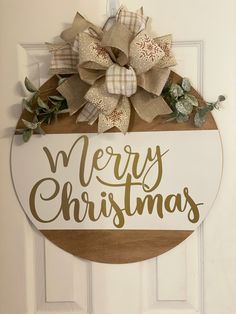 a merry christmas sign hanging on the front door with a large bow and greenery