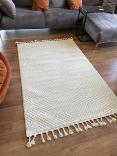 a white rug with tassels is on the floor in front of a gray couch