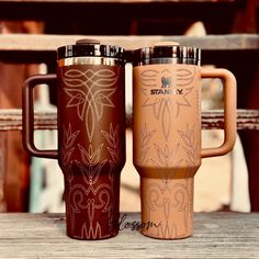 two travel mugs sitting on top of a wooden table