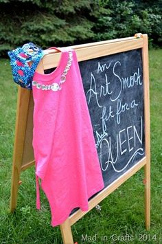 a pink shirt hanging on a sign in the grass next to a blue hat and purse