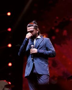 a man in a suit and tie holding a microphone to his face while standing on stage