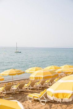 many yellow umbrellas and chairs on the beach near the water with a boat in the distance