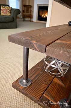 a wooden table with metal legs in front of a fire place and couch behind it