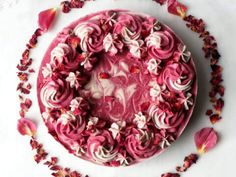 a cake with pink frosting and flowers around it on a white tablecloth surrounded by petals