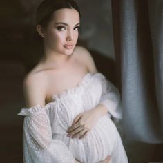 a pregnant woman is posing for the camera with her arms wrapped around her waist and wearing a white dress