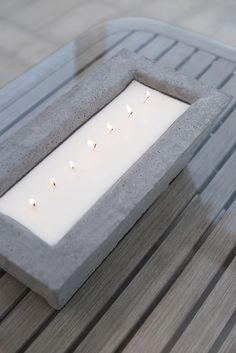 some candles are lit in a concrete box on a wooden table with slatted boards