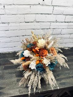 a bridal bouquet with feathers and flowers on a wooden table in front of a brick wall