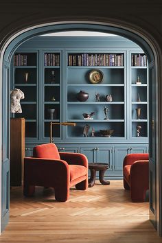 an archway leads into a library with blue bookshelves and orange chairs in it