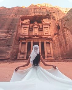 a woman in a white dress is standing in front of an ancient building