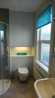 a white toilet sitting next to a bath tub in a bathroom under a window with blue roller shades