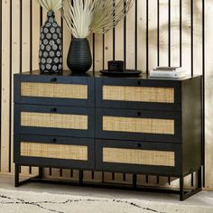 a black dresser with wicker drawers and vases on top, against a striped wall