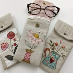 three handmade glasses cases with embroidered flowers on them, one has a pair of eyeglasses and the other two are made out of linen