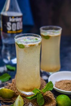 two glasses filled with liquid and limes on a table