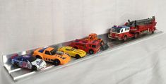 several toy cars are lined up on a metal shelf in front of a white backdrop