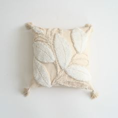 a white pillow with leaves on it and tassels hanging from the back side