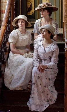 three women in dresses and hats sitting on stairs