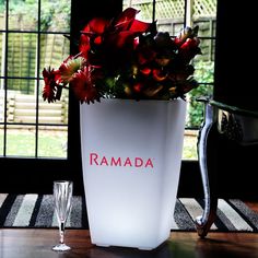 a white vase with red writing on it sitting next to a wine glass and some flowers