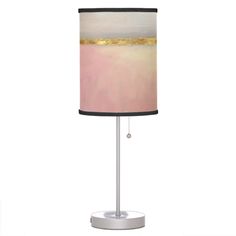 a table lamp with a pink and gold shade on the bottom, sitting on a white base