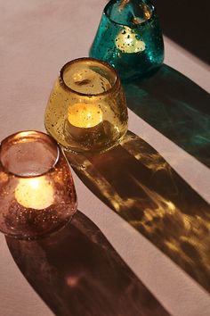 three glass candles sitting on top of a table next to each other with their shadows