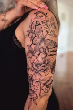 a woman's arm with flowers and butterflies on it, while she is holding her hand up to her shoulder