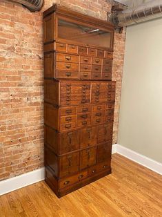 an old wooden filing cabinet sitting in front of a brick wall with exposed pipes on the ceiling