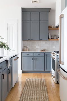 a kitchen with gray cabinets and white counter tops, hardwood floors, and a rug on the floor