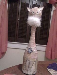 a cat statue sitting on top of a table in front of a window with pink curtains