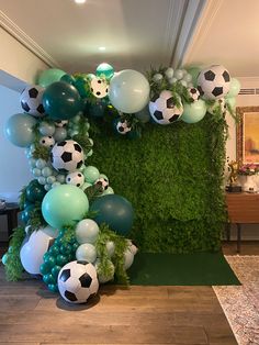 an arrangement of balloons and soccer balls in the shape of a heart on a green wall