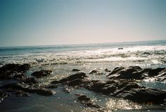 the sun shines on some rocks in the water at the beach near the ocean