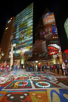 people are walking in the city at night with brightly lit buildings and colorful carpets on the ground