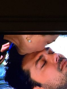 a man and woman kissing each other while laying on the bed in front of a tv