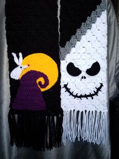 two crocheted scarves with faces on them, one is white and the other is black