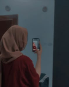 a woman in a red shirt is taking a selfie with her cell phone while wearing a headscarf