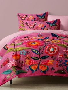 a bed covered in pink comforter next to a wall with butterflies and flowers on it