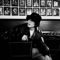 black and white photograph of a woman sitting in a chair with pictures on the wall behind her