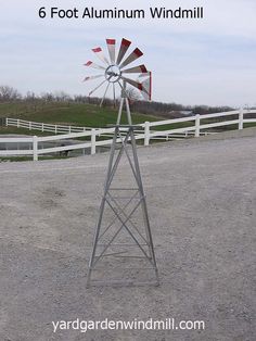 a metal windmill sitting in the middle of a dirt field next to a white fence