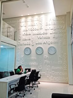 a man sitting at a desk in an office with clocks on the wall