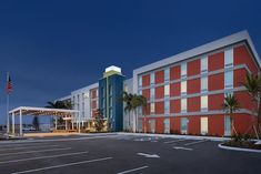 an empty parking lot in front of a hotel at night with palm trees and lights