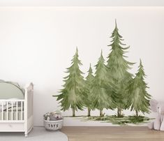 a baby's room with a crib, bed and wall decal that has trees painted on it