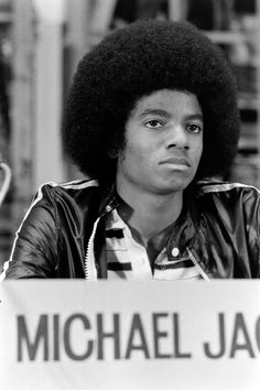 a man with an afro sitting at a table in front of a sign that says michael jackson