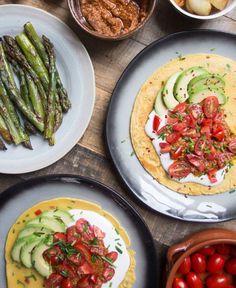 plates with different types of food on them sitting on a table next to bowls of tomatoes, asparagus and other vegetables