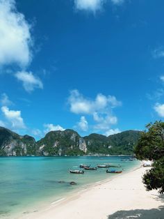 there are many boats that are on the water at this beach and some mountains in the background