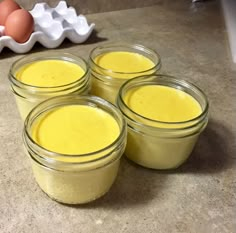 four jars filled with yellow liquid sitting on top of a counter next to an egg