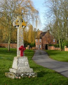 a stone cross with red flowers on it in the middle of a grassy area next to a road