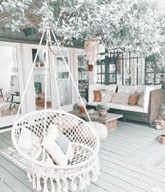 a white hanging chair on a porch next to a couch and coffee table with pillows