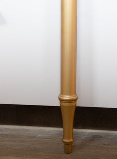 a tall gold metal pole sitting on top of a hard wood floor next to a white wall