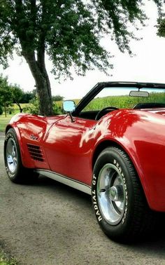 a red sports car is parked on the side of the road next to a tree